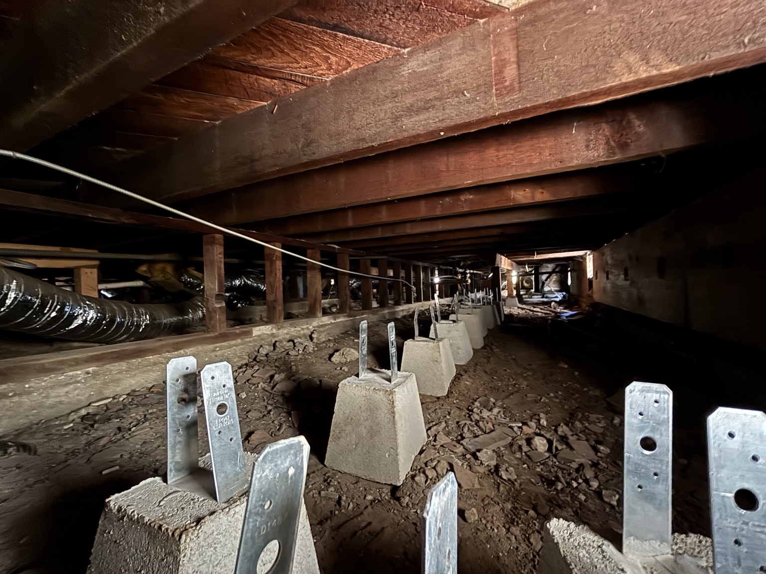New support pier brackets beneath floor framing in crawl space