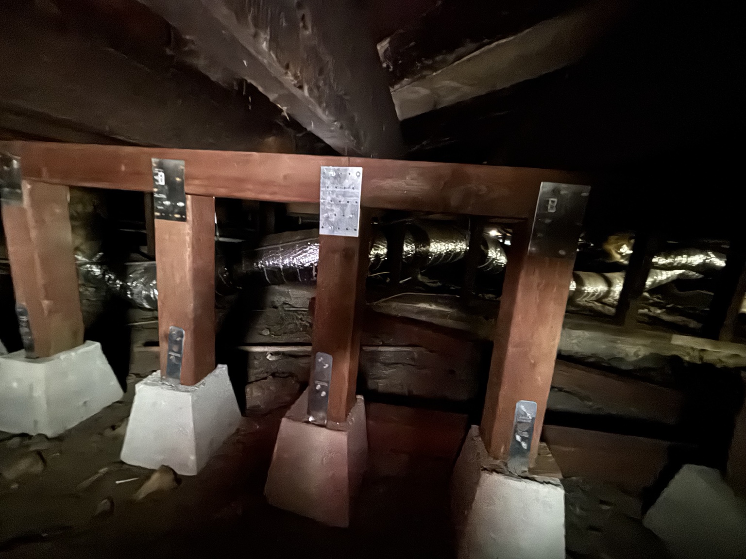 Wood posts and metal connectors supporting floor beam below the house