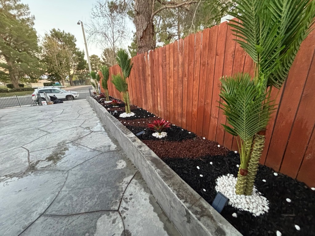 Completed planting bed with palm trees, dark mulch, white decorative stones and lights