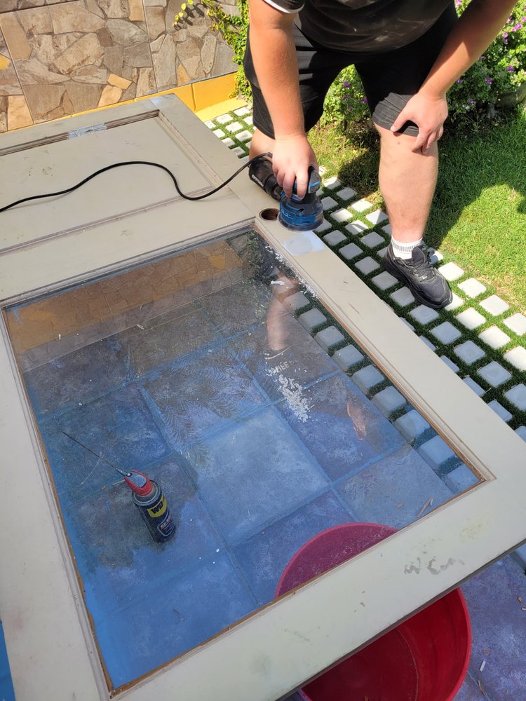 Sanding a door surface around its glass panel during preparation for refinishing